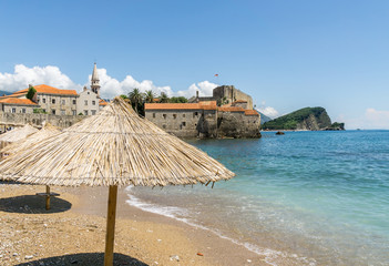 Straw umbrellas on Budva Old Town Beach in Budva, Montenegro, with the Stari Grad (Old Town) in the background.