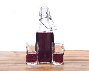 Homemade raspberry liqueur in clear glass bottle with swing top and shot glass on bamboo table