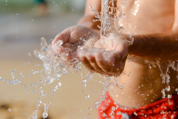 Fototapeta premium Closeup on child hand catching water. Splashing drops on sunny summer outdoors background.