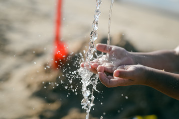 Closeup on child hand catching water. Splashing drops on sunny summer outdoors background.