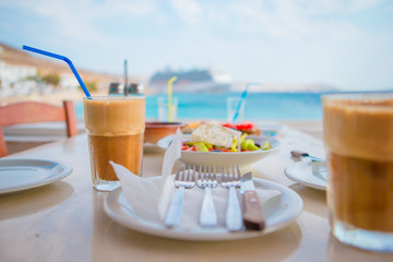 Frappe on the table background sea and big lainer. Summer iced coffee frappuccino in a tall glass and greek salad in beach bar