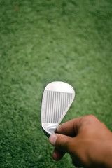 Closeup of a golfers hand using golf club, green grass background