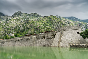 Fototapeta na wymiar Kampana Tower and Citadel, the World Heritage listed fortifications surrounding the medieval village of Kotor in Montenegro reflected in the Skurda River, with mountains in the background.