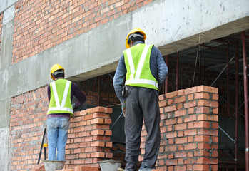 MALACCA, MALAYSIA -OCTOBER 14, 2016: Construction workers laying clay brick to form brick wall at the construction site. The bricks stick using cement mortars. 