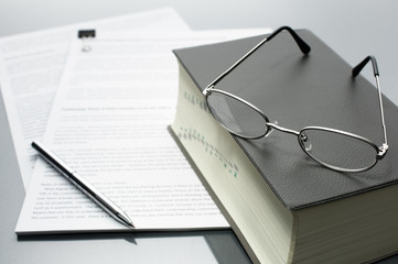 Reading and checking documents with a dictionary. Documents, dictionary, glasses and pen on gray...