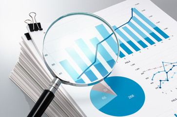Reviewing and analyzing business reports. Magnifying glass and pile of documents. 
