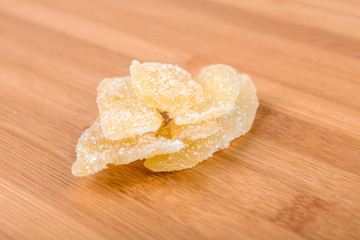 Stack of crystallized ginger pieces isolated on wood background