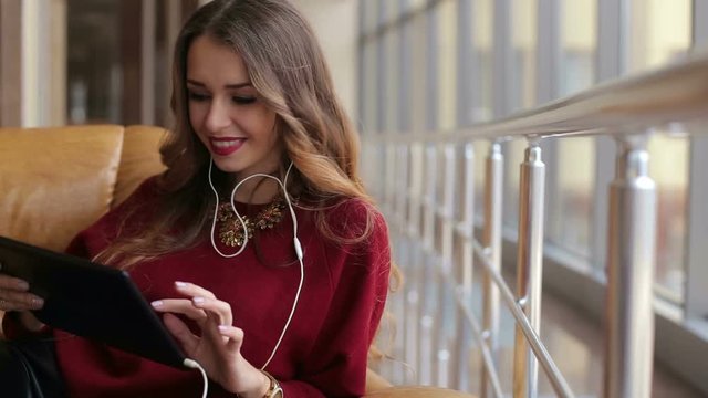 Attractive young girl sitting at the airport in a chair and listening to the music through headphones. Beautiful girl with headphones. Young girl with tablet.