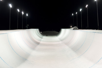 Snowboarder in a snow halfpipe at night lit up by lights