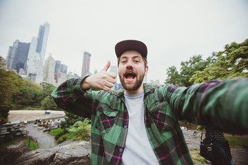 Handsome bearded hipster taking selfie with camera in Central Park, New York. Happy student makes...