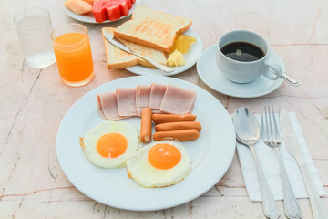 Breakfast with Fried egg, Ham, Sausage, toast, jam, butter, water melon, orange juice and black coffee on marble table.