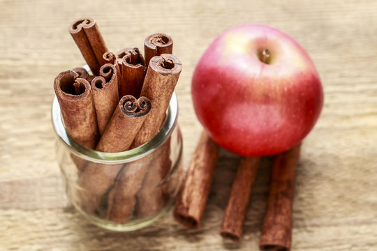 Cinnamon sticks and red apple on wood