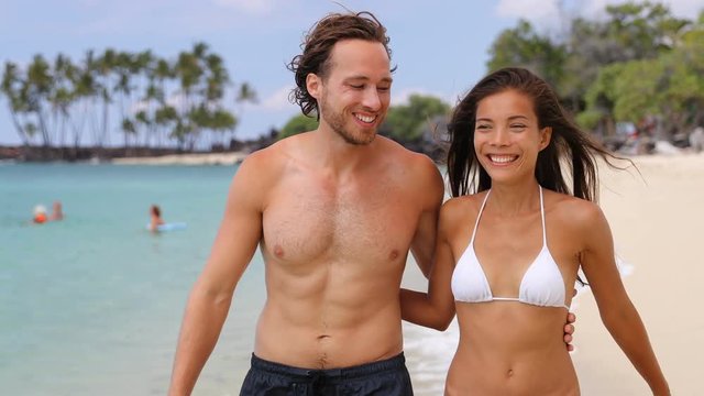 Beautiful sexy suntan people. Happy young interracial couple with slim and fit body relaxing walking on tropical paradise beach during summer vacation holiday. Travel relaxation sun honeymoon concept.