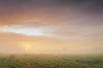 Sunrise over a misty meadow with straw blocks