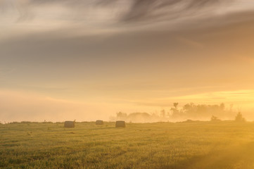 Sunrise over a misty meadow with straw blocks