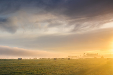 Fototapeta na wymiar Sunrise over a misty meadow with straw blocks
