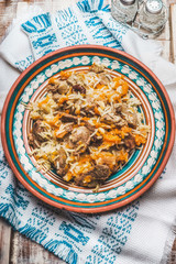 Rice with meat and vegetables in rustic plate on rustic background with embroidery napkin. Pilaf, national dish, top view