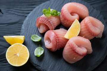 Closeup of marinated tilapia rolls with lemon and green basil