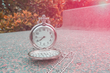Silver pocket watch on a stone chair in the park.