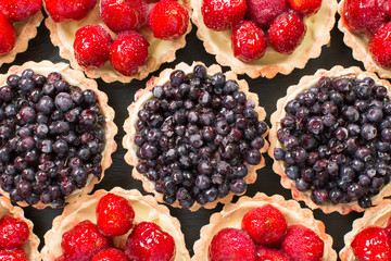 Fresh summer blueberries nd strawberries in a tartlets on a wood