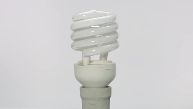Rotating vertical spiral fluorescent light bulb in holder on white background