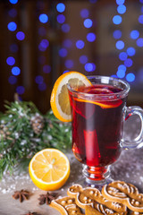 Mulled wine with lemon and cinamon sticks in glass and christmas cookies on the wooden table with christmas tree branch and snow