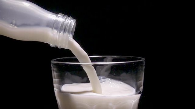 Milk pouring in glass from bottle in slow motion. Close up with black background.