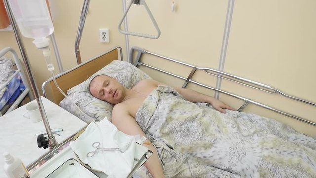 View of intravenous drip and a male patient lying on bed in the background