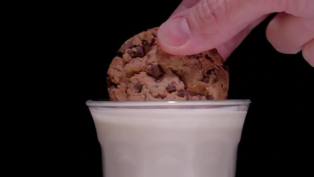 Dunking chocolate chip cookie in glass of milk, slow motion flm clip. Close up with black background.