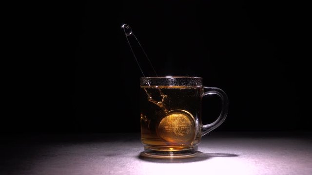 Pouring hot water in glass teacup from transparent teapot. 