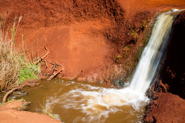 Ein Wasserfall gräbt sich durch rotes Gestein im Waimea Canyon, Kauai, Hawaii, USA.