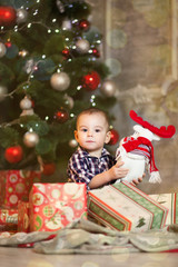 Fototapeta na wymiar A little boy sitting under the Christmas tree with toys and gifts