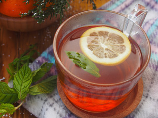 Herbal tea in a glass cup and teapot, fresh mint leaves, a napkin on a wooden boards background