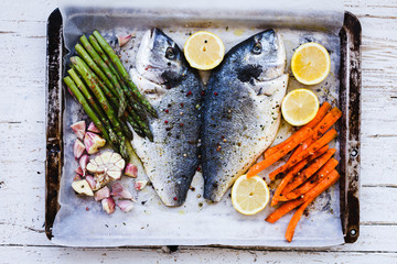 Fresh fish with aromatic herbs, asparagus and carrots, lemon sliced and condiments ready for baking.