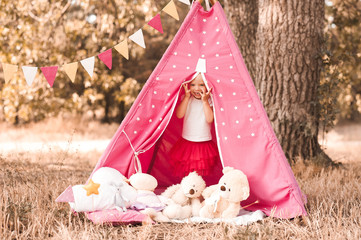 Smiling baby girl 3-4 year old hiding with toys in wigwam outdoors. Playful. Childhood. © morrowlight
