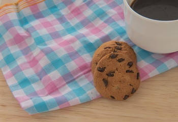 Chocolate chip cookie on a cloth and coffee on wood background.