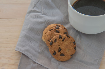 Chocolate chip cookie on a cloth and coffee on wood background.