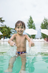 Naklejka premium Young boy kid child splashing in swimming pool having fun leisur