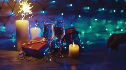 Process of setting fire a sparkler over Christmas decor with candles, gift boxes and two flutes of champagne background