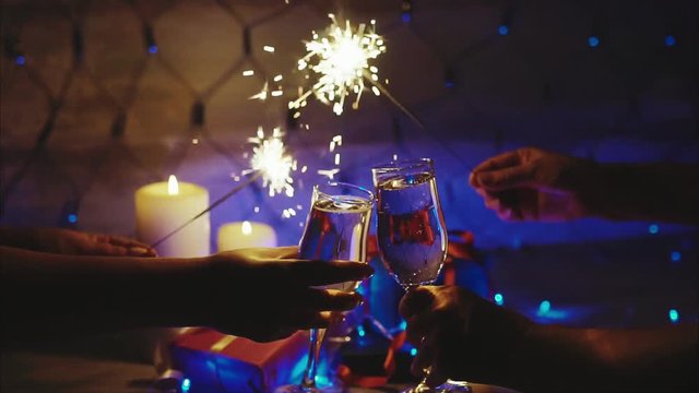 Couple toasting with champagne christmas scene and sparkler bokeh blinking background slow motion close up