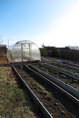 Obraz premium Handmade polycarbonate greenhouse and garden beds in the April garden against a blue sky
