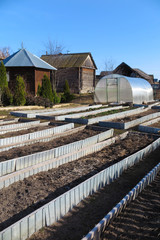 Garden beds and a handmade polycarbonate greenhouse in the April garden against a blue sky