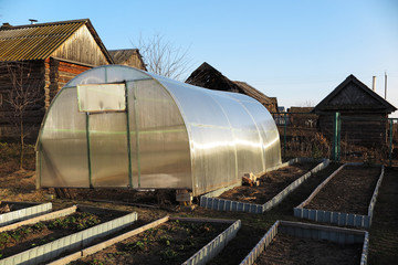 Handmade polycarbonate greenhouse and garden beds in the April garden against a blue sky