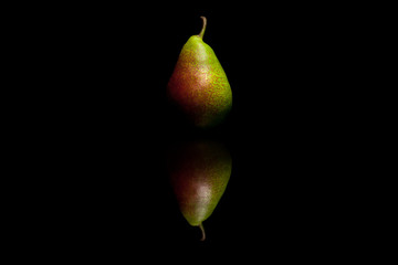 One whole red and green pear isolated on black reflective backgr