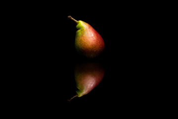 One whole red and green pear isolated on black reflective backgr