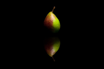One whole red and green pear isolated on black reflective backgr