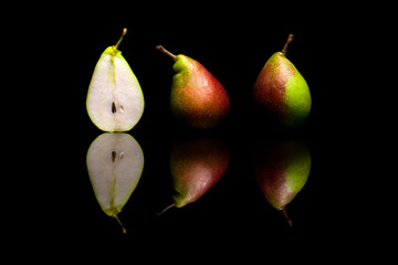 One cut in half and two whole red and green pears isolated on bl
