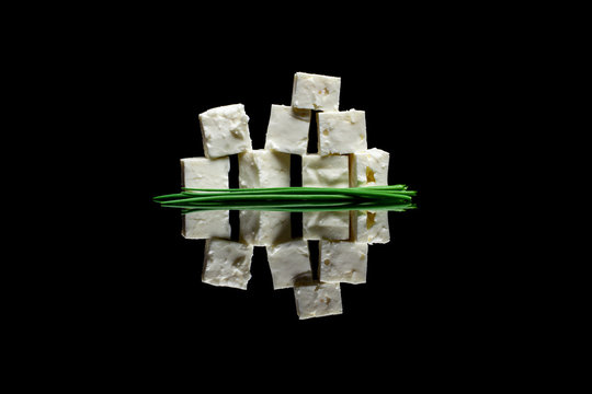Eight blocks of feta cheese with whole green chive on black back