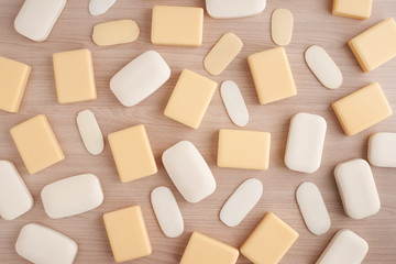 Твердое мыло на деревянном фоне. Бруски мыла и остатки мыла разбросаны на столе. Мыло белого и желтого цвета.