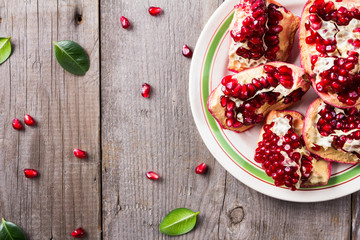 Broken red ripe juicy pomegranates in the white plate on rustic wooden unpainted table